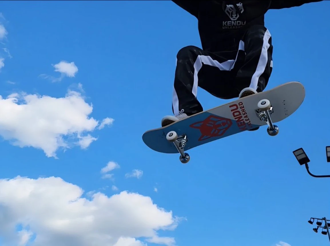 Skateboarder airborne against a blue sky with a Kendu Unleashed deck